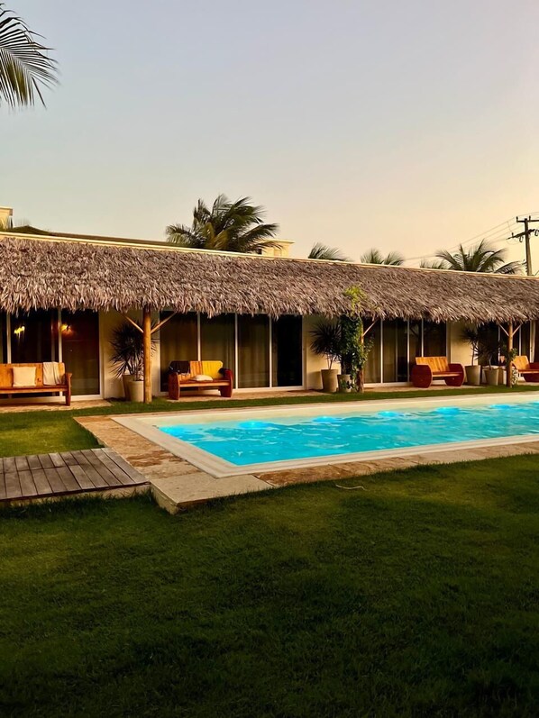 A poolside area with a thatched-roof building, outdoor seating, and a swimming pool. - Pousada Vila Flow (Caucaia)