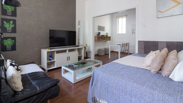 A modern living room with a flat-screen TV, a glass coffee table, a sofa, and a bed with a blue bedspread. - Refuge in Copacabana for two | NSC1011 (Rio de Janeiro)