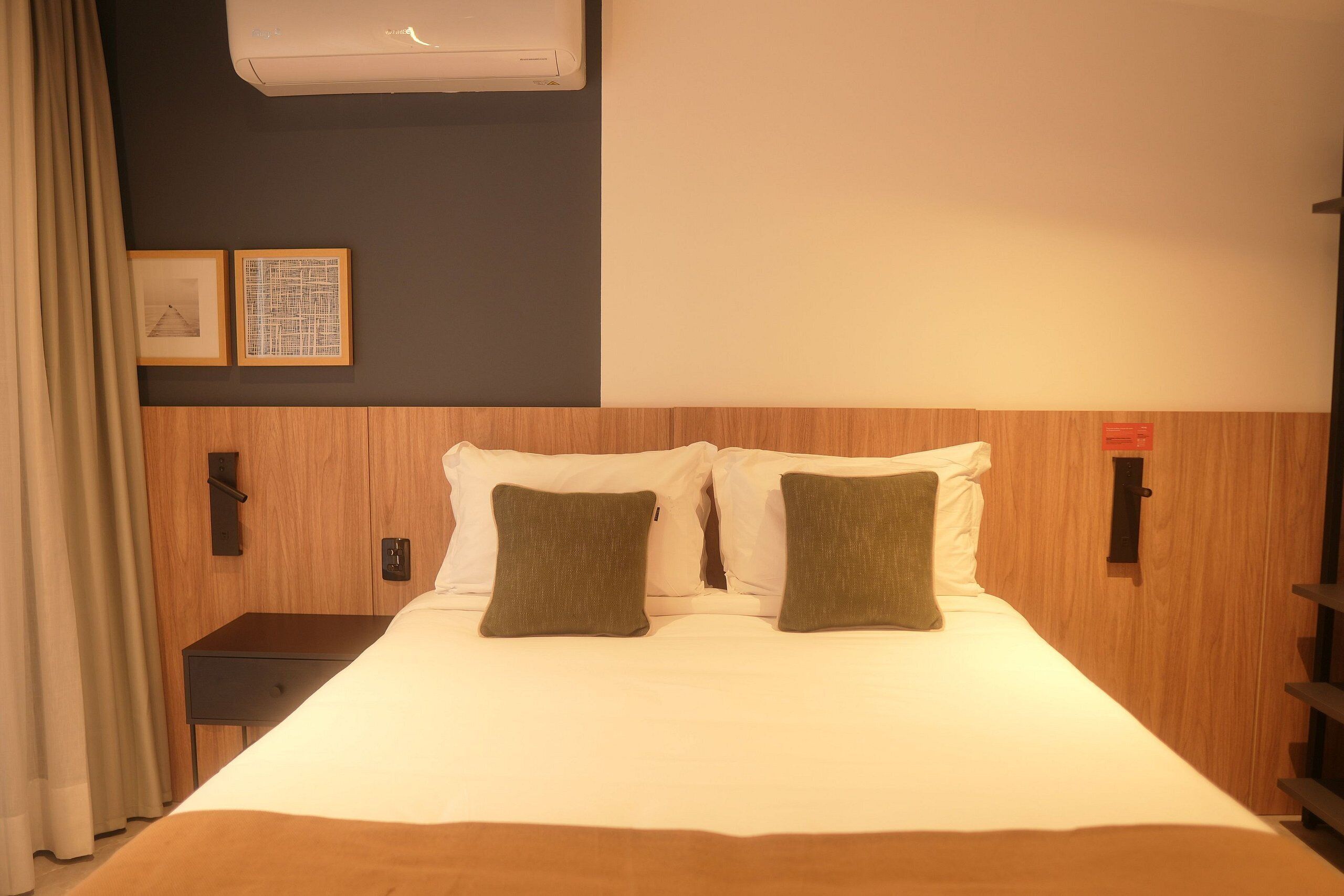 A hotel room with a bed, a nightstand, and a wall-mounted air conditioner.