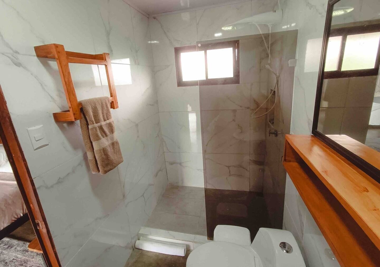 Un bagno con doccia vetrata, porta asciugamani in legno e WC bianco.