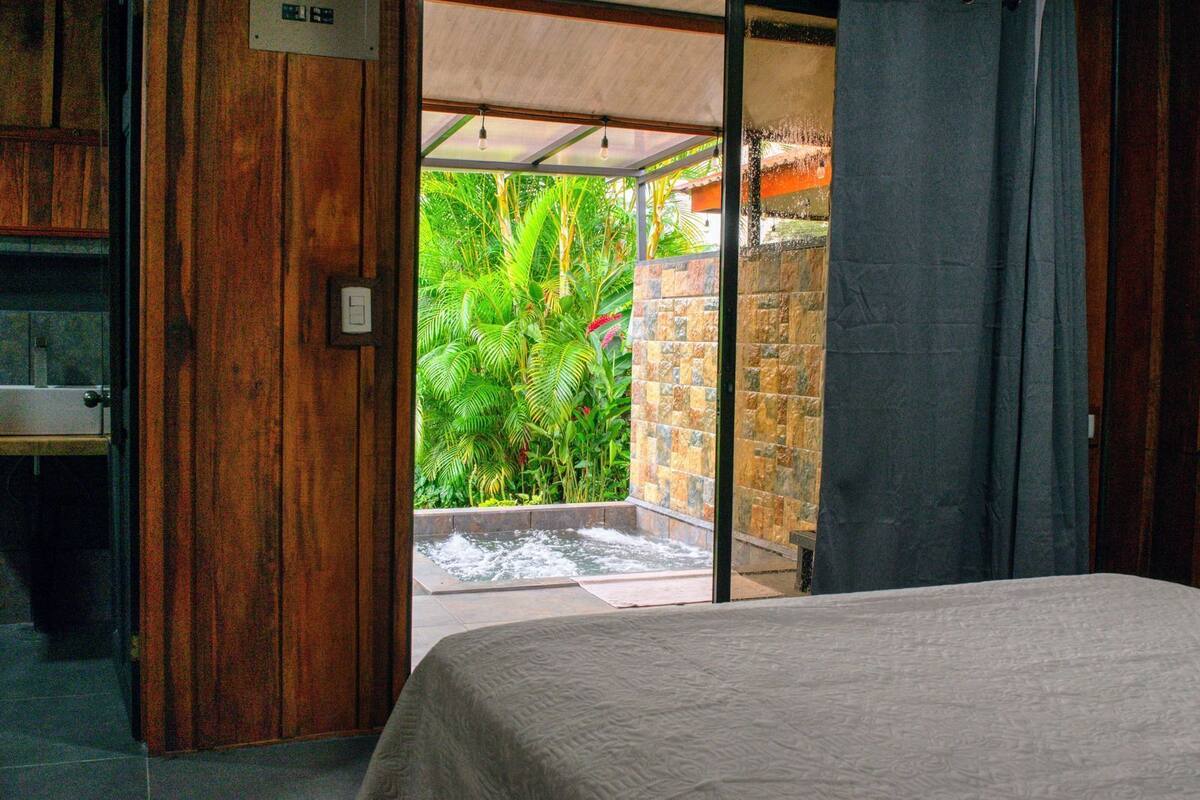 A bedroom with a bed, a sliding glass door leading to a small outdoor area with a water feature and lush greenery.