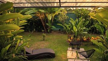 A covered outdoor area with a grass lawn, two lounge chairs, and a small table.
