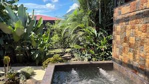 Un jardin agrémenté d’un élément aquatique, de plantes tropicales luxuriantes et d’un mur en briques.