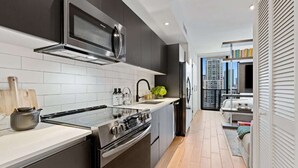 A modern kitchen with dark cabinetry, a stainless steel range hood, and a large window offering a city view. - Luxury Living | Unmatched Bay Views & VIP Perks (Miami)