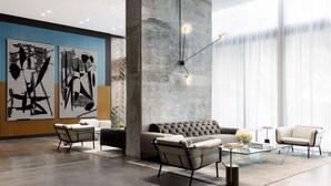 A modern lobby with a large abstract artwork, a grey sofa, two armchairs, a glass coffee table, and a minimalist light fixture. - Luxury Living | Unmatched Bay Views & VIP Perks (Miami)