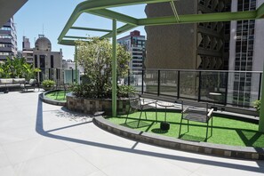 A rooftop terrace with a green metal pergola, seating areas, and a small garden.