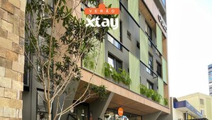 Edifici modern amb una escala que condueix a una entrada amb teulada verda, envoltat de vegetació exuberant.