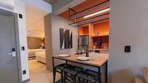 Een compacte hotelkamer met kitchenette, een zithoek met tafel en stoelen, en een bed op de achtergrond.