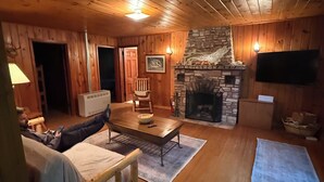 A cozy cabin interior with a stone fireplace, wooden walls, a television, and a comfortable seating area.
