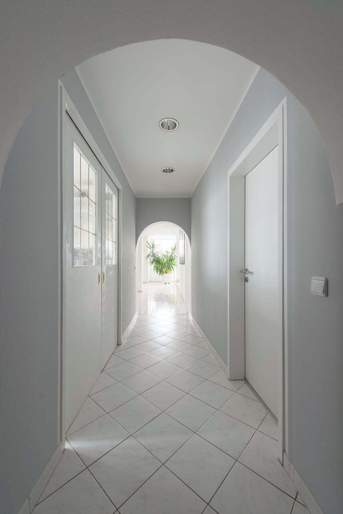 A hallway with white walls, a tiled floor, and a door at the end.