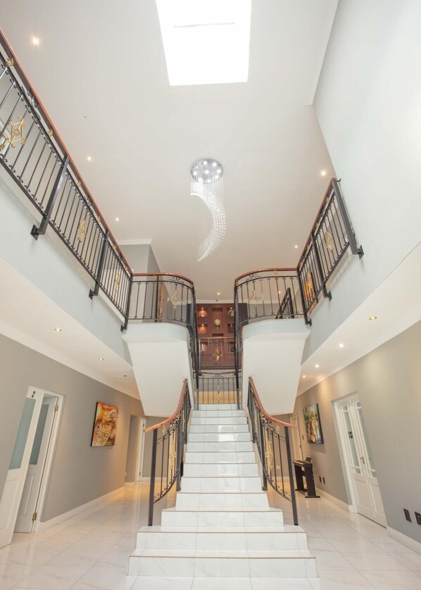 A spacious, multi-level interior with a central staircase, polished marble floors, and modern lighting fixtures. - Adinkra Boutique Hotel (Randburg)
