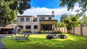 A two-story house with a well-maintained lawn, outdoor seating, and a large window overlooking the yard. - Adinkra Boutique Hotel (Randburg)