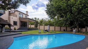 Una piscina con borde curvo, un porche cubierto y un edificio con balcón.
