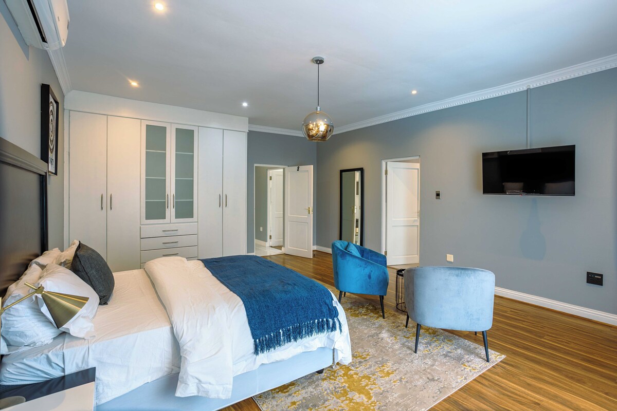 A modern bedroom with a large bed, a blue armchair, a television, and a wardrobe.