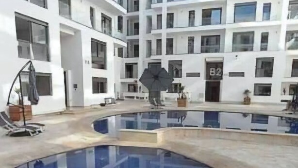 Une piscine au design incurvé, entourée d’un bâtiment blanc doté de nombreuses fenêtres et de balcons.