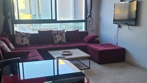 Un salon moderne avec un canapé rouge, une table basse en verre et un téléviseur à écran plat fixé au mur.