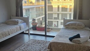 Une chambre avec deux lits, une grande fenêtre et une vue sur un bâtiment à l’extérieur.