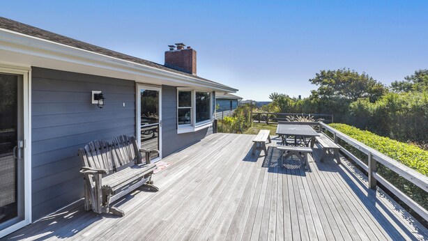 Une terrasse en bois avec un banc et une table de pique-nique, donnant sur un jardin et un plan d’eau.