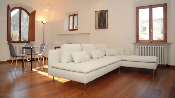 Ein modernes Wohnzimmer mit einem weißen Modulsofa, einem Esstisch mit Stühlen und großen Fenstern mit Holzrahmen.