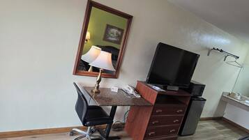 A hotel room with a desk, chair, television, and a mirror.