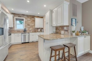 Une cuisine avec des meubles blancs, un plan de travail en granit et deux tabourets en bois.