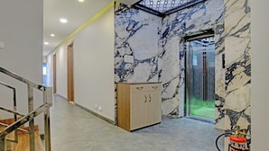 A hallway with marble walls, a wooden cabinet, and an elevator. - Hotel Shiv Chhaya (Indore)