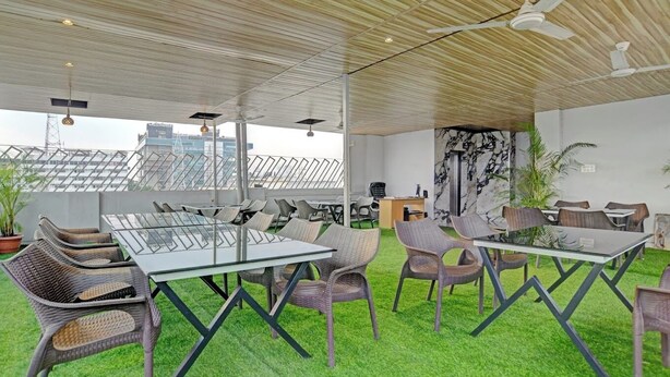 A modern meeting room with glass tables and wicker chairs, a ceiling fan, and a view of buildings through large windows. - Hotel Shiv Chhaya (Indore)