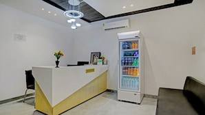 A reception area with a white reception desk, a glass refrigerator stocked with beverages, and a modern chandelier. - Hotel Shiv Chhaya (Indore)