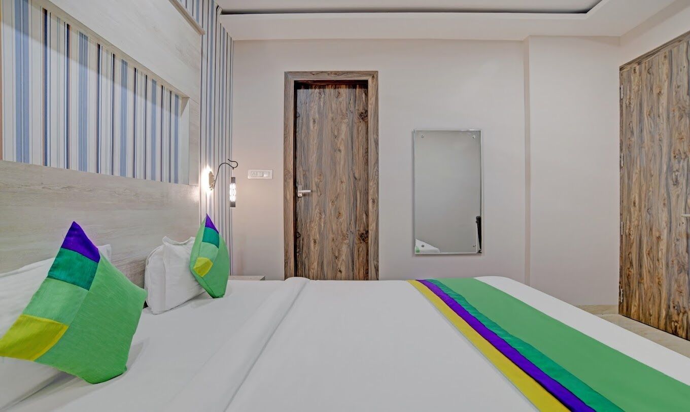 A hotel room with a bed, pillows, a wooden door, and a mirror on the wall.