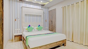 A modern bedroom with a wooden bed frame, striped wallpaper, and a large window with curtains. - Hotel Shiv Chhaya (Indore)