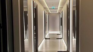 Ein langer, gut beleuchteter Korridor mit Marmorboden, Notausgangsschildern und Türen an beiden Seiten.