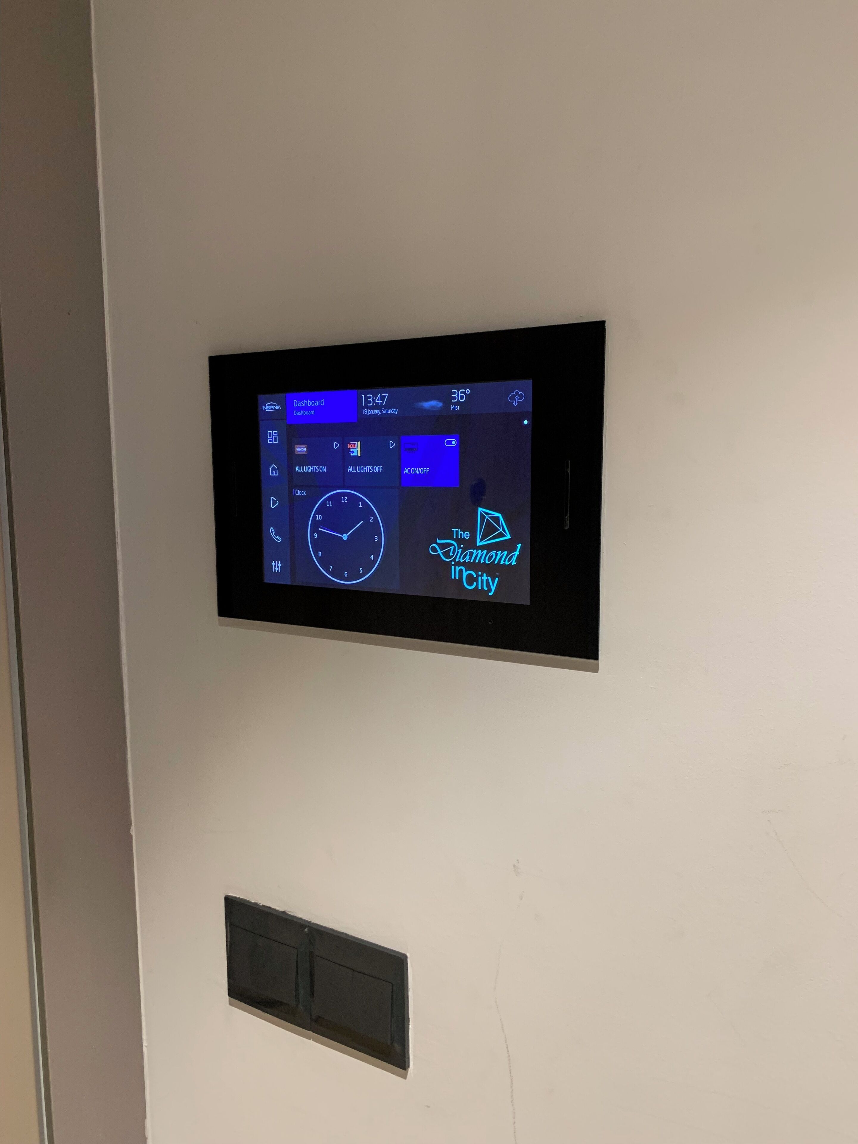 A digital display on a wall with a clock, a weather widget, and a logo for "The Diamond City".