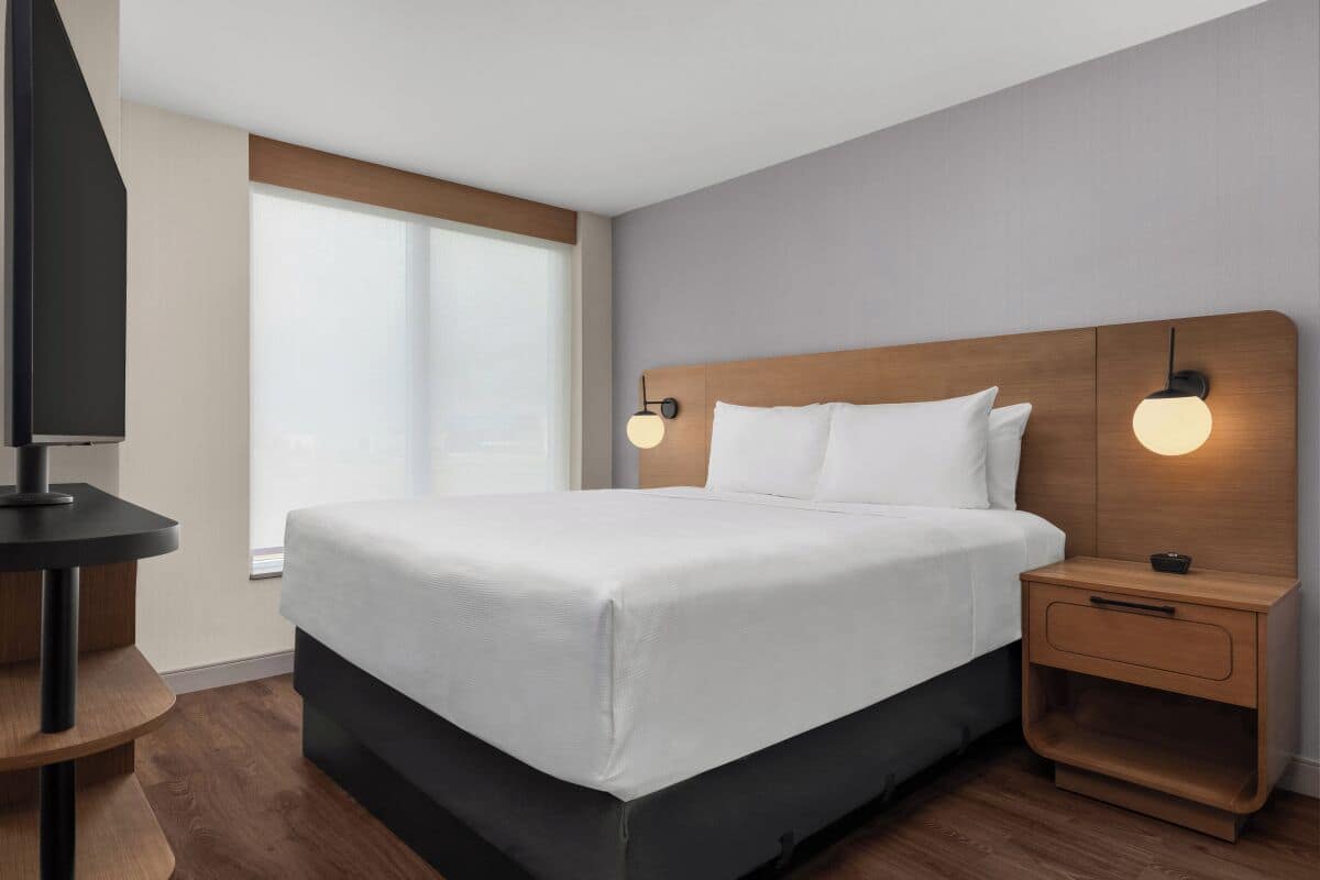 Ein modernes Hotelzimmer mit einem großen Bett, einem Holzkopfteil, Nachttischen und einem Fernseher auf einem Schrank.