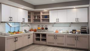 A modern kitchen with light wood cabinets, a glass backsplash, and a variety of kitchen appliances and utensils.