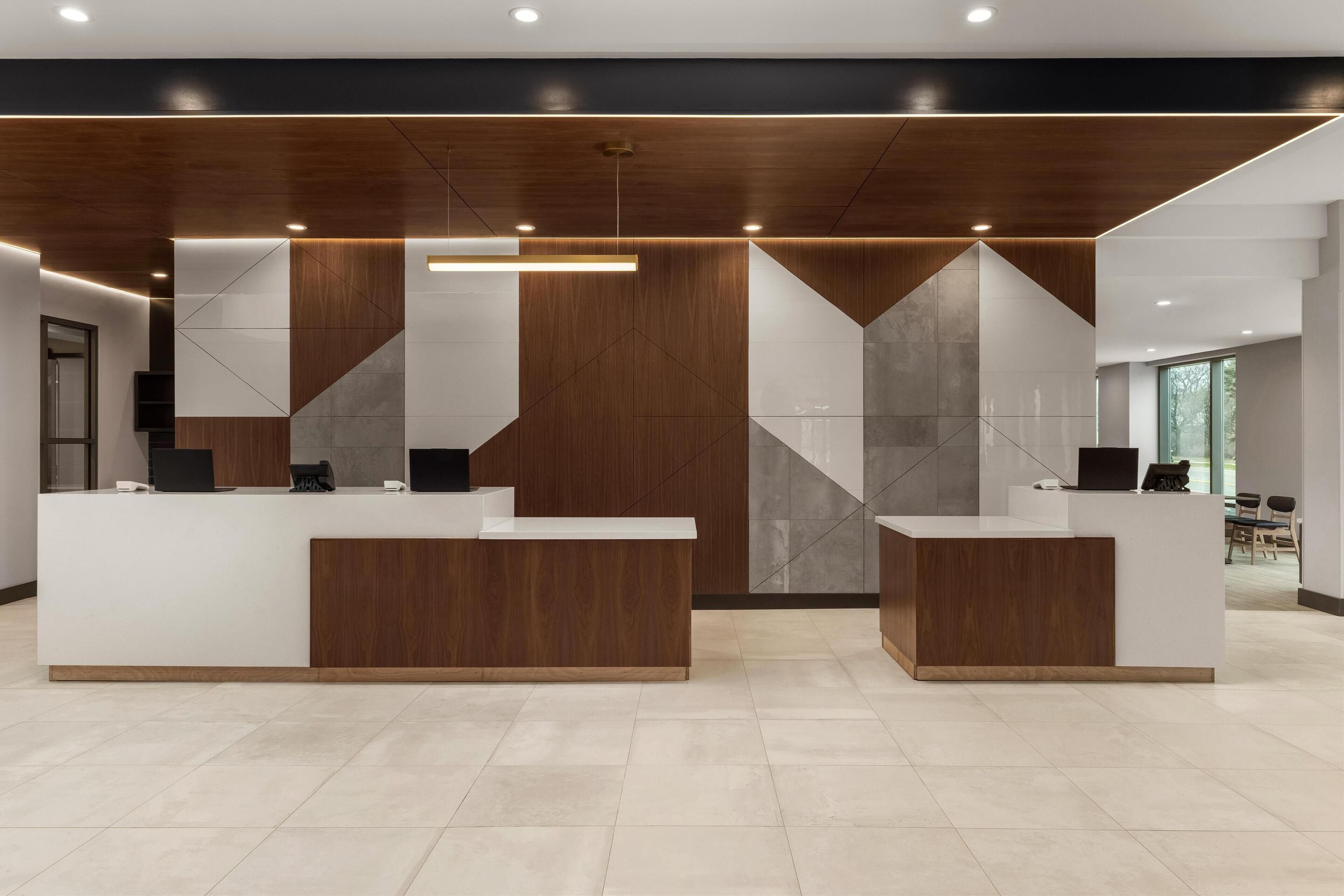 Un espace d’accueil doté de deux comptoirs de réception blancs, d’éléments décoratifs en bois et d’un motif géométrique sur le mur.