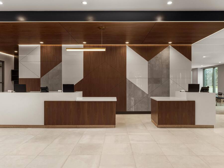 Un espace d’accueil doté de deux comptoirs de réception blancs, d’éléments décoratifs en bois et d’un motif géométrique sur le mur.