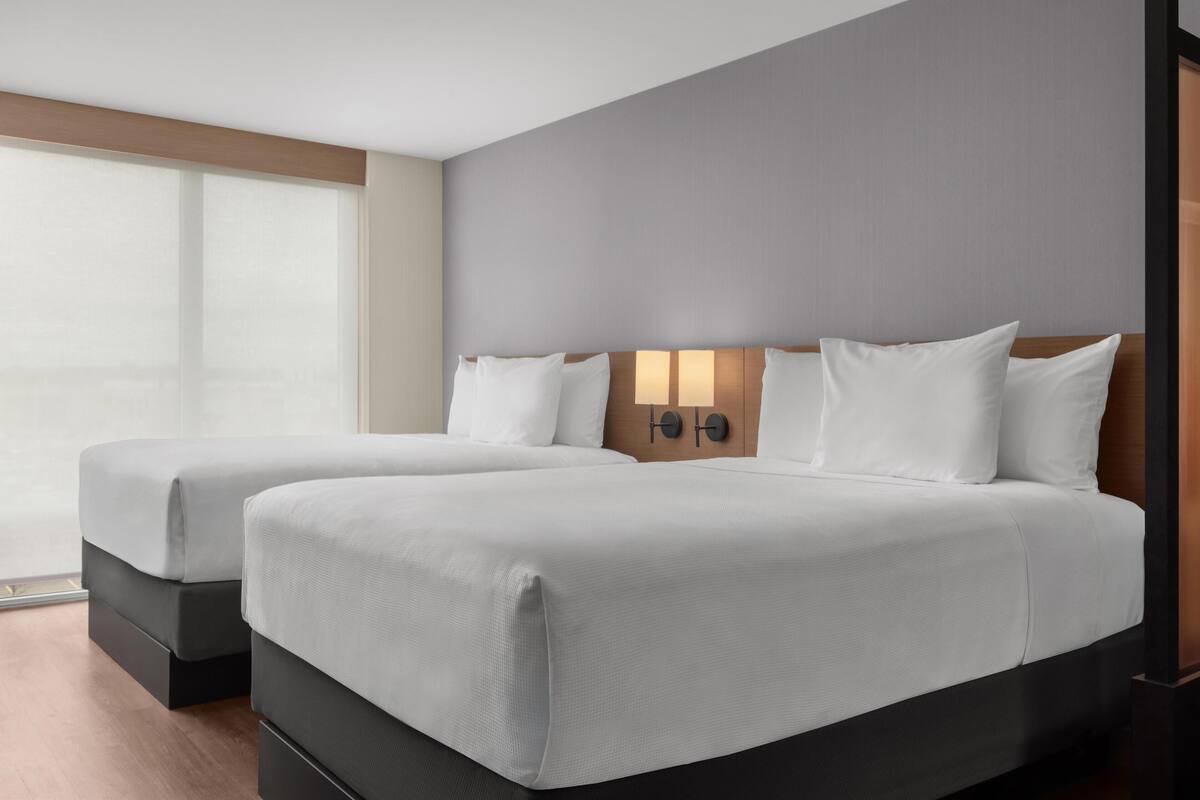 Ein Hotelzimmer mit zwei Betten, einem großen Fenster und einer Wandleuchte.