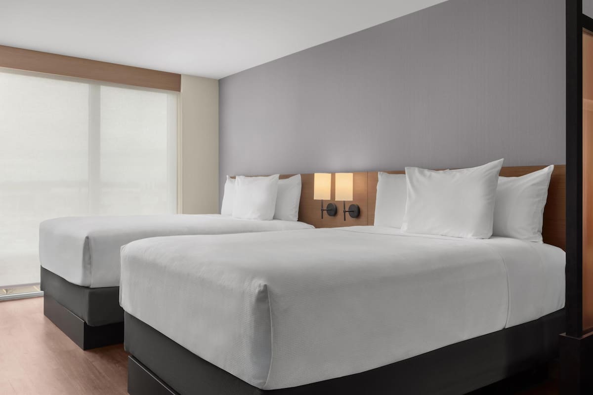 Une chambre d’hôtel avec deux lits, une grande fenêtre et un luminaire fixé au mur.