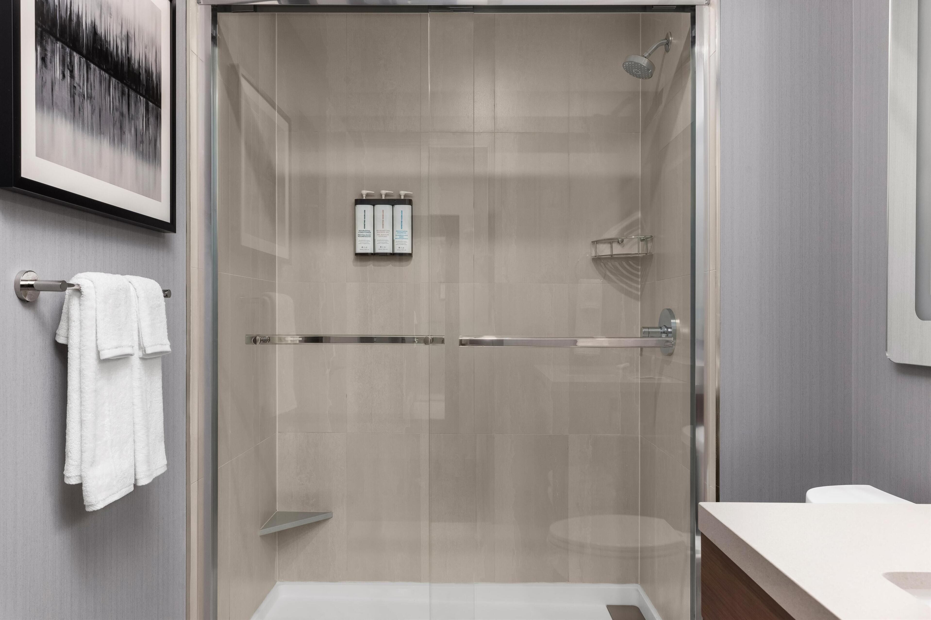 A modern bathroom with a glass-enclosed shower, a white sink, and a towel rack.