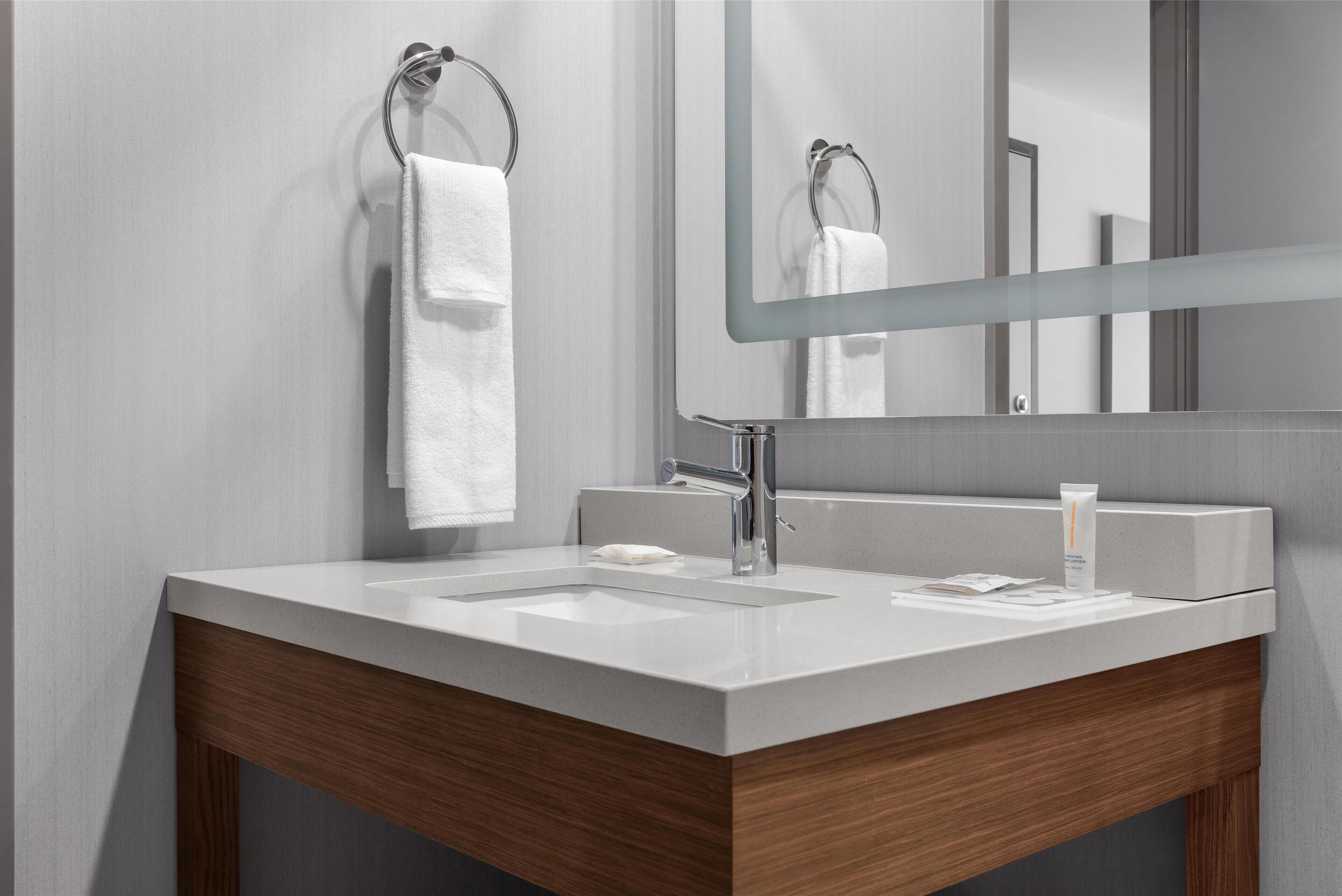 Un baño moderno con un lavamanos blanco, un espejo y un mueble de tocador de madera.