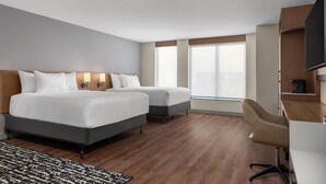 A hotel room with two beds, a desk, a chair, and a television.