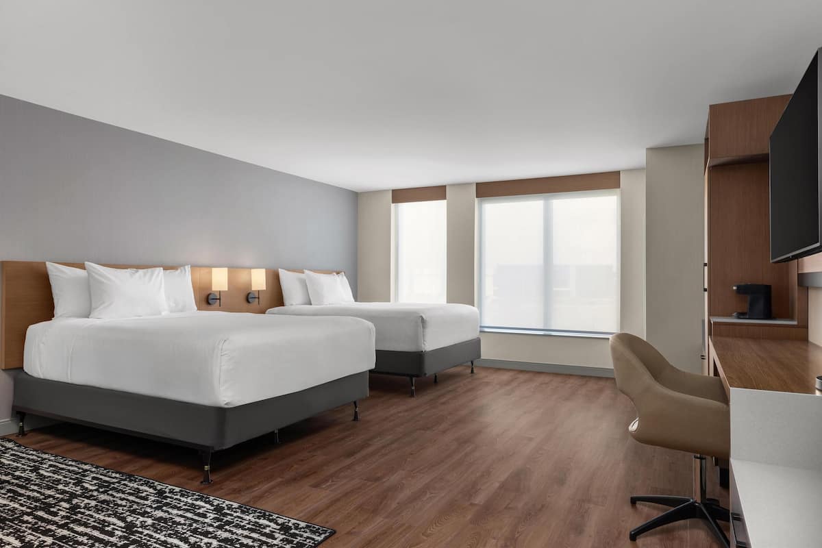 Ein Hotelzimmer mit zwei Betten, einem Schreibtisch, einem Sessel und einem Fernseher.