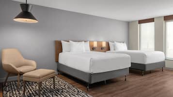 A hotel room with two beds, a chair, a small table, a patterned rug, and a hanging light fixture.