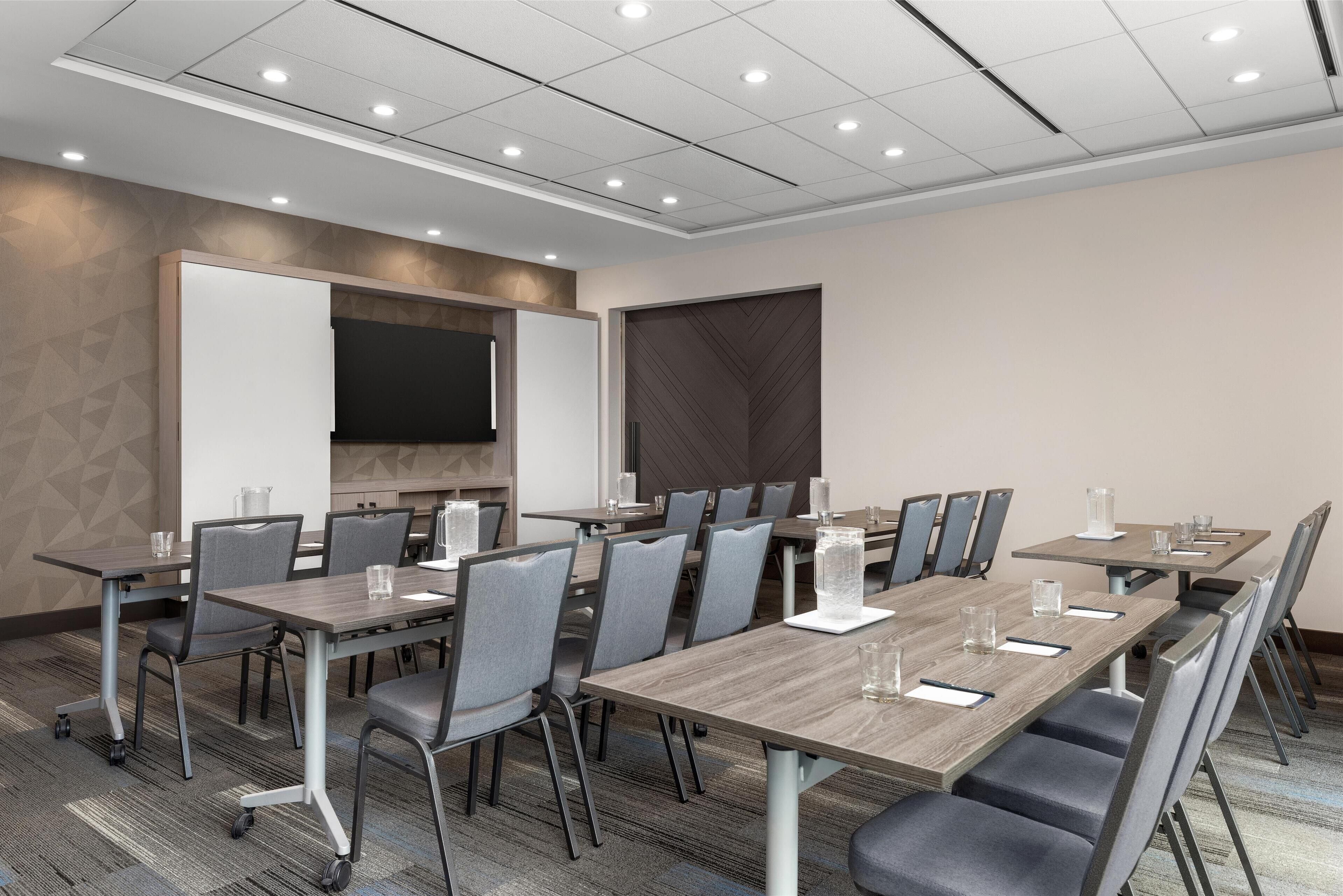 A conference room with a long table, chairs, a whiteboard, and a large screen.