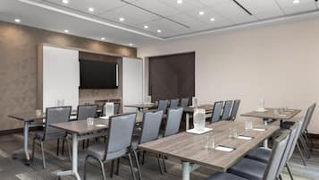 A conference room with a long table, chairs, a whiteboard, and a large screen.