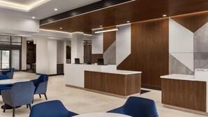 A modern reception area with a wooden reception desk, blue chairs, and a white table.