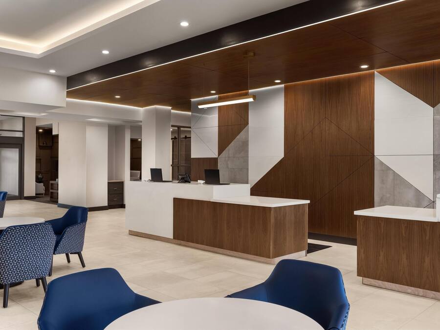 A modern reception area with a wooden reception desk, blue chairs, and a white table.