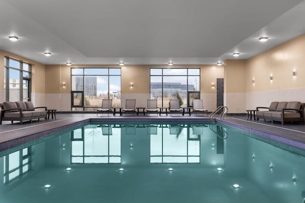 A large indoor swimming pool with multiple lounge chairs and a view of buildings in the background.