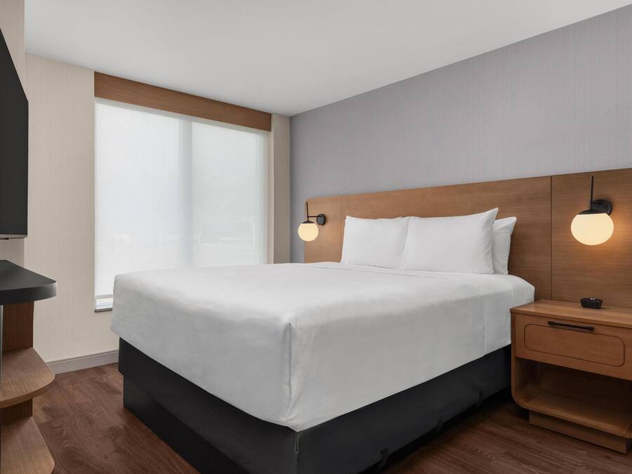 Habitació d'hotel moderna amb un llit gran, un panell de capçalera de fusta, taules de nit i un televisor sobre un suport.
