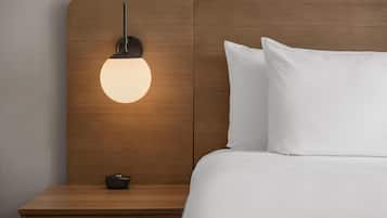 Una cama bien hecha con sábanas blancas, cabecera de madera y mesita de noche con lámpara.